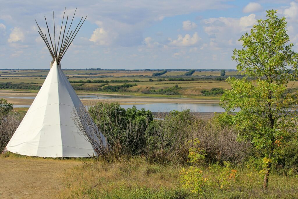 A picturesque teepee by a tranquil lake in Saskatchewan, Canada under a blue sky.